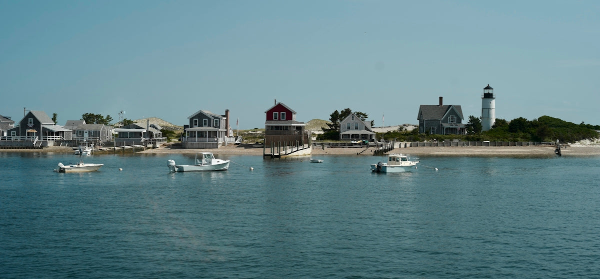 Boats float near a coastal town with a lighthouse.