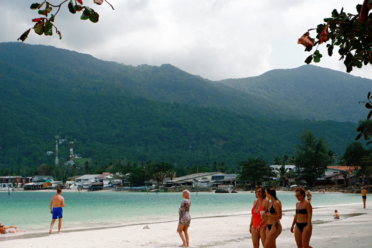 People on a sandy beach with mountains in background.