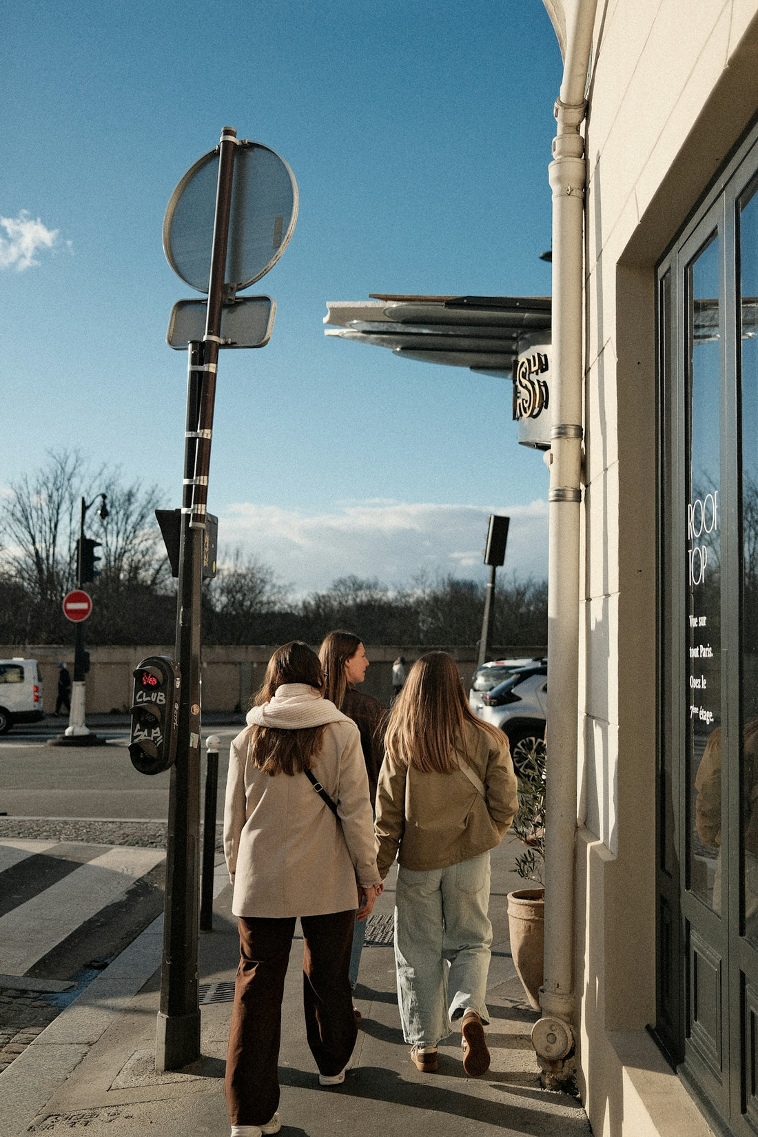 Three young women walk down a sunny street.